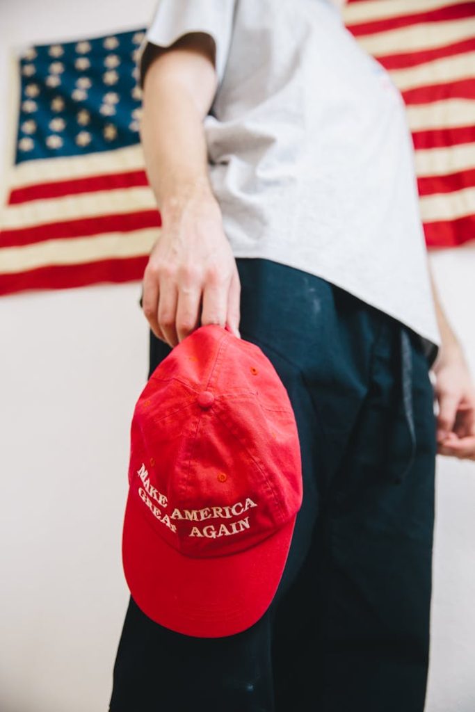 A person holding a Make America Great Again hat against a backdrop of the American flag.